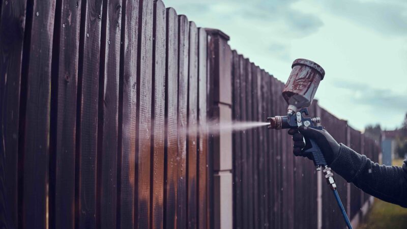 man-n-protective-gloves-is-applying-paint-old-fence-using-airbrush-his-garden_11zon